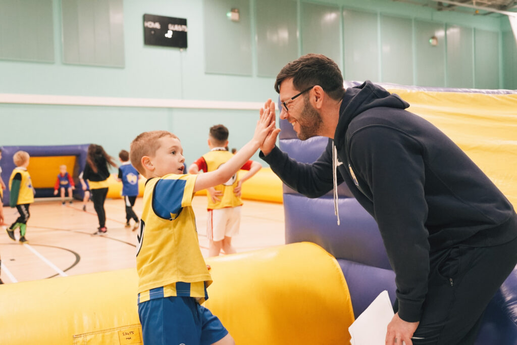 Smiling Football Fun Factory Coach giving a child a high-five.