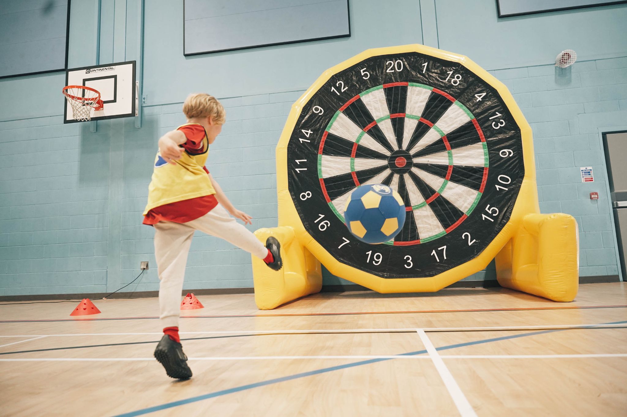 A child kicking a ball at a giant inflatable dartboard
